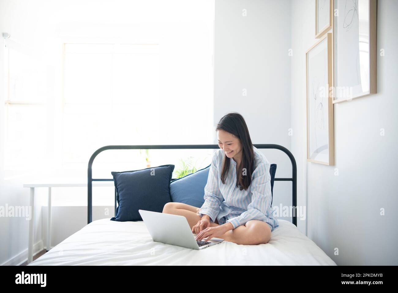 Eine Frau im Pyjama, die einen Computer auf dem Bett berührt Stockfoto