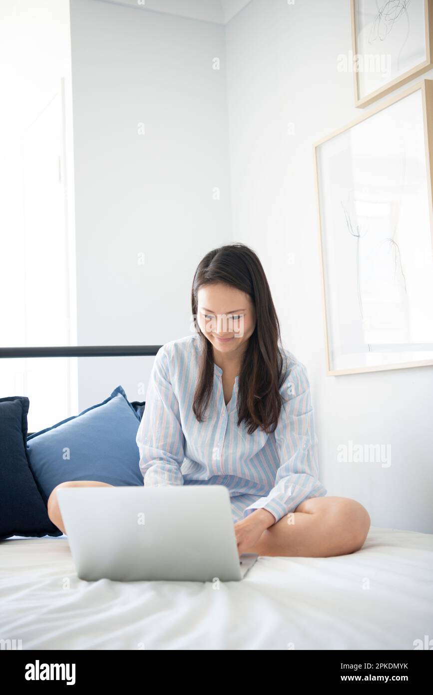 Eine Frau im Pyjama, die einen Computer auf dem Bett berührt Stockfoto