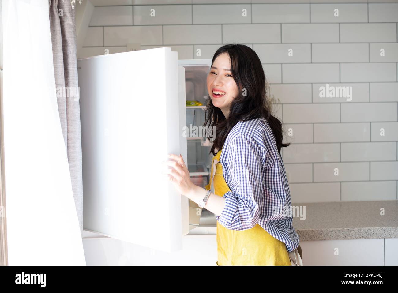 Frau mit Schürze in der Küche, die den Kühlschrank öffnet Stockfoto