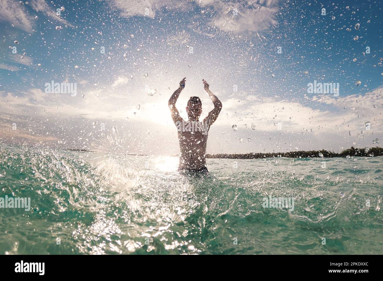 Silhouette eines fröhlichen Mannes, der im Meer steht und Wasser in die Kamera spritzt. Sonniger Tag im tropischen Reiseziel während des Strandurlaubs. Stockfoto