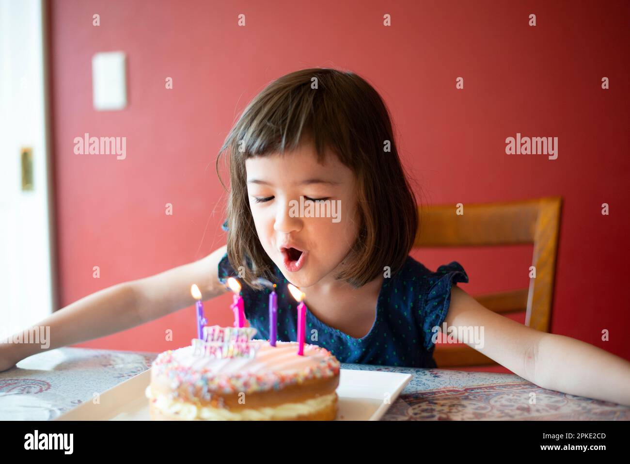 Mädchen bläst Kerzen auf Kuchen Stockfoto