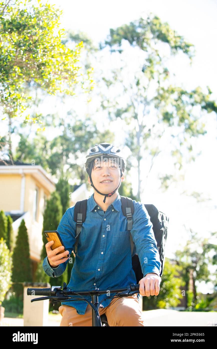 Liefermann, der auf einem Fahrrad mit einem Smartphone unterwegs ist Stockfoto