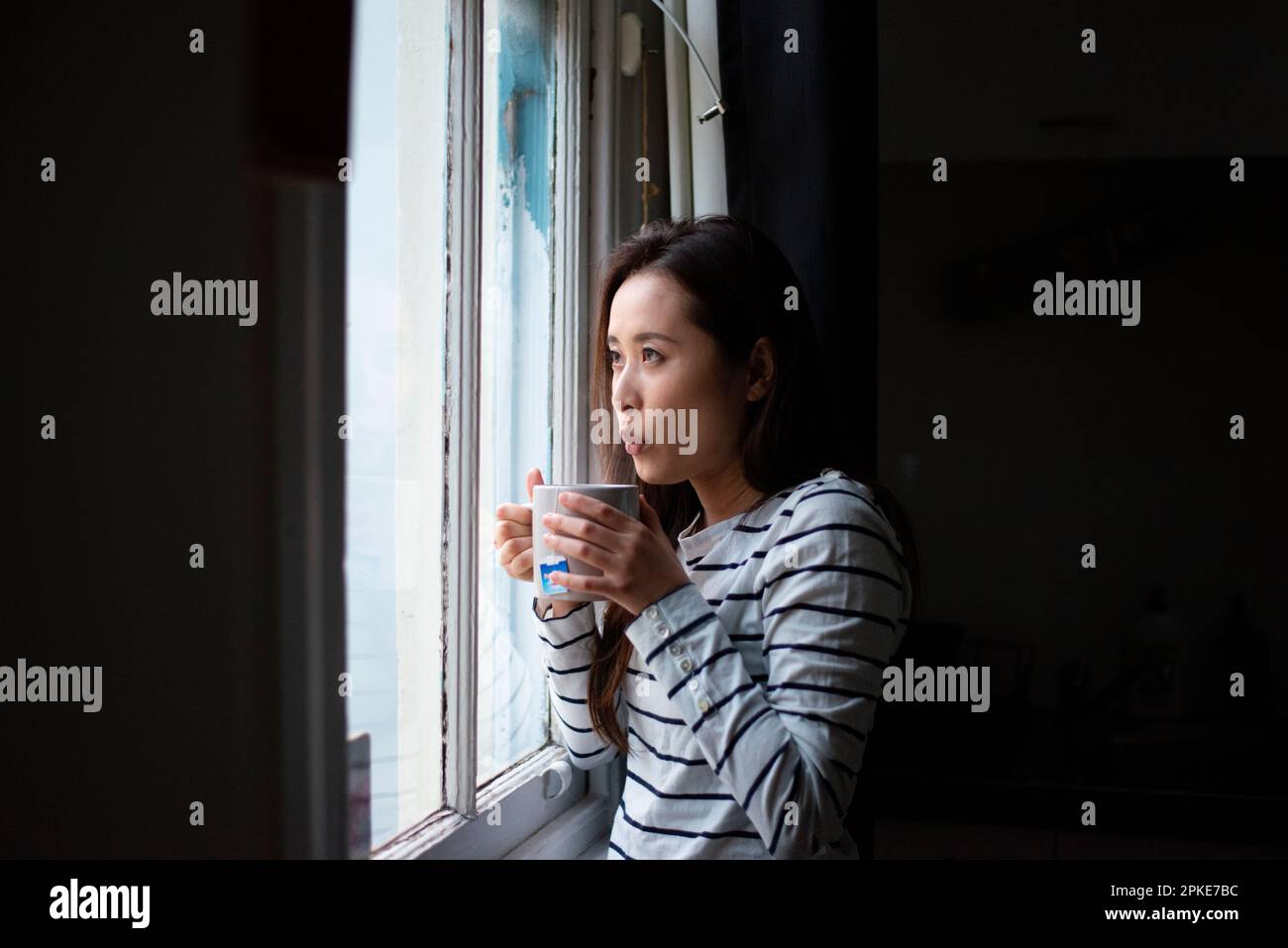 Frau mit einem warmen Drink am Fenster Stockfoto