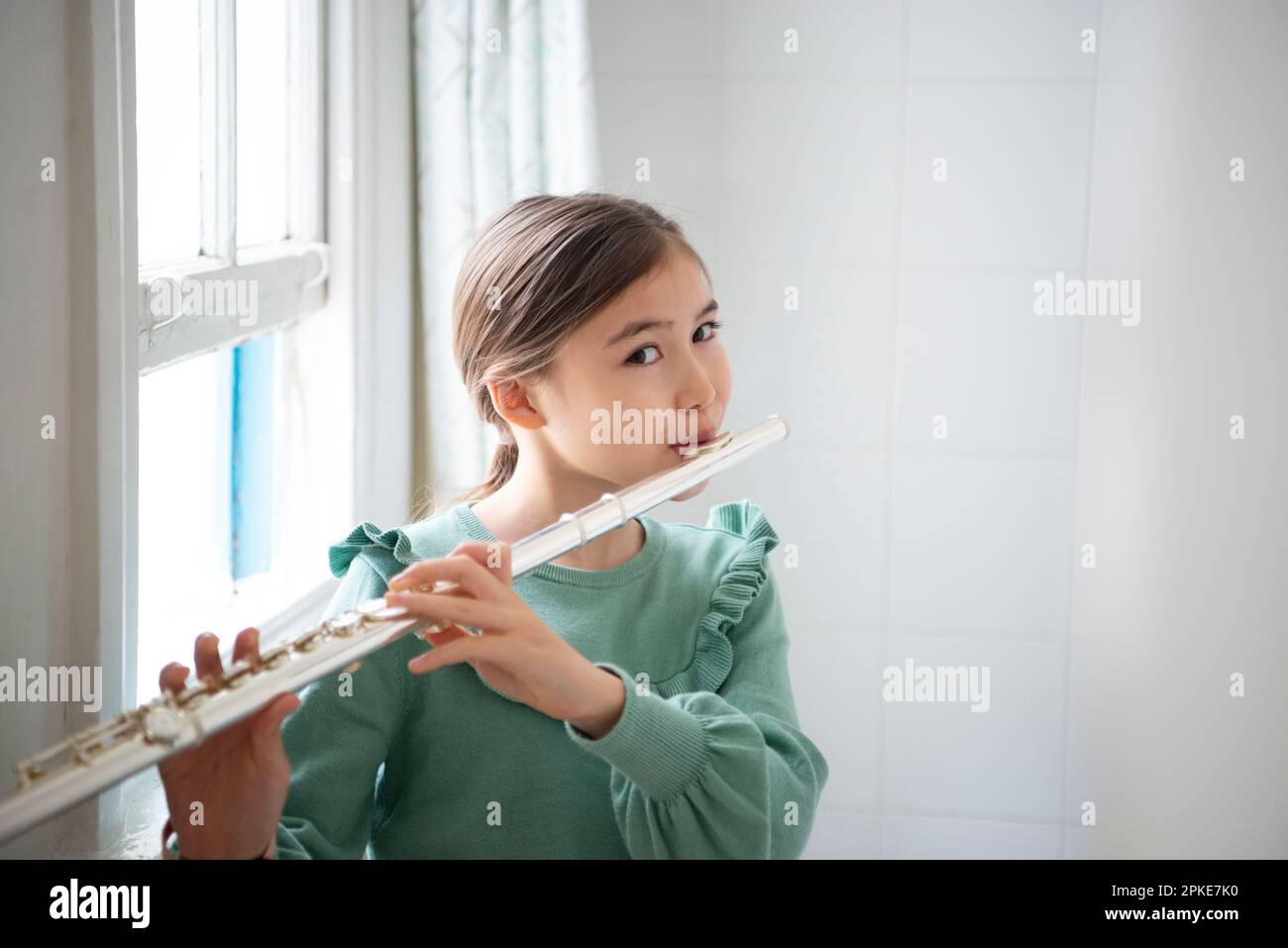 Ein Mädchen, das Flöte am Fenster spielt Stockfoto