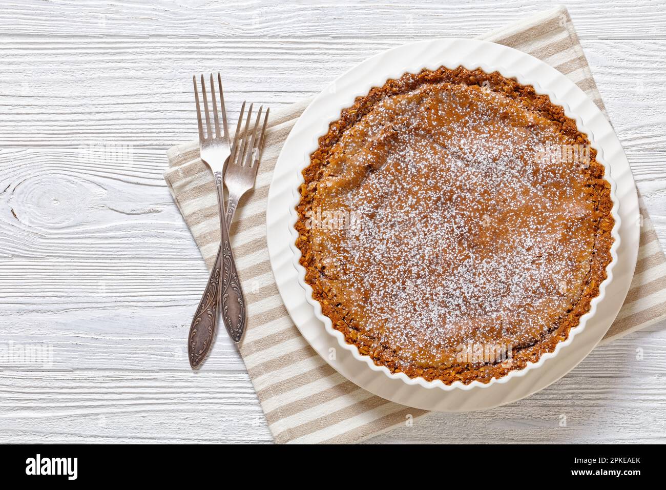 Milk Bar Crack Pie mit knuspriger Haferkruste und leckerer Füllung mit Süßwaren, weißer Backform auf weißem Holztisch mit Iforks, horizontal Stockfoto