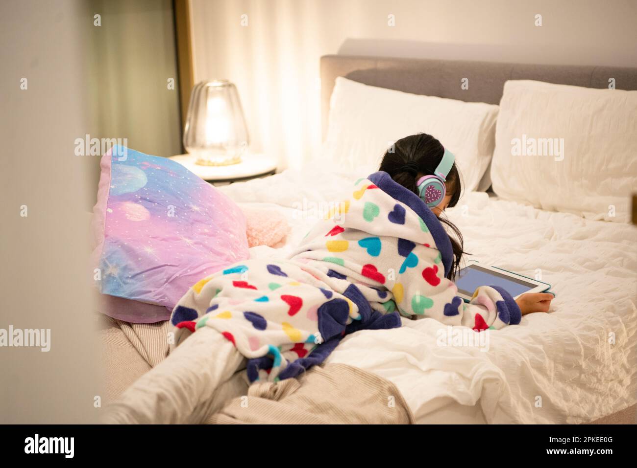 Ein Mädchen, das auf dem Bett liegt und ein Tablet mit Kopfhörern ansieht Stockfoto