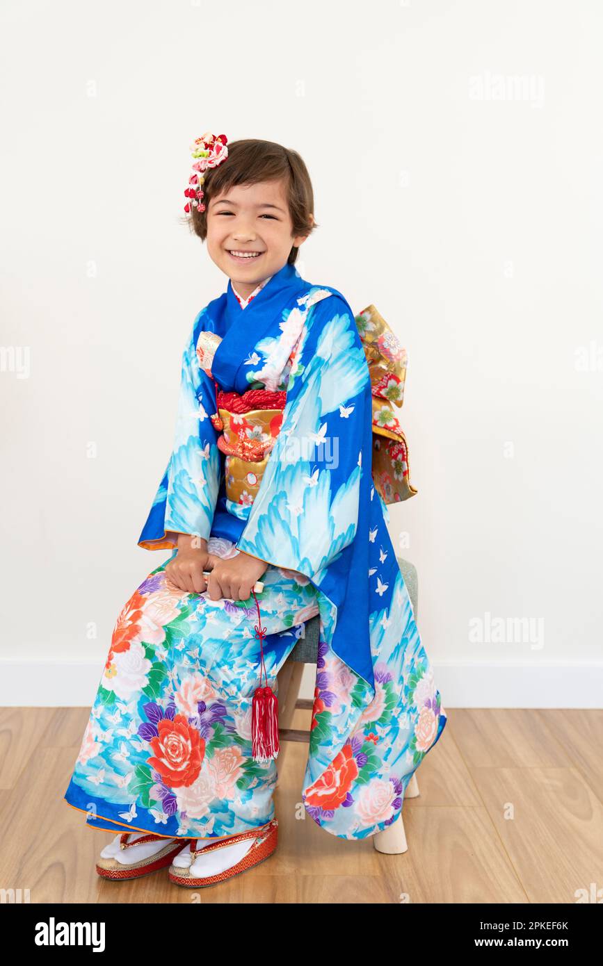 Ein Mädchen in 753 Kimono, das lachend auf einem Stuhl sitzt Stockfoto