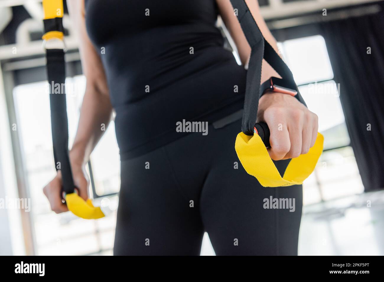 Zugeschnittene Ansicht einer Seniorin in schwarzer Sportbekleidung, Training mit Aufhängebändern im Fitnessstudio, Stockbild Stockfoto