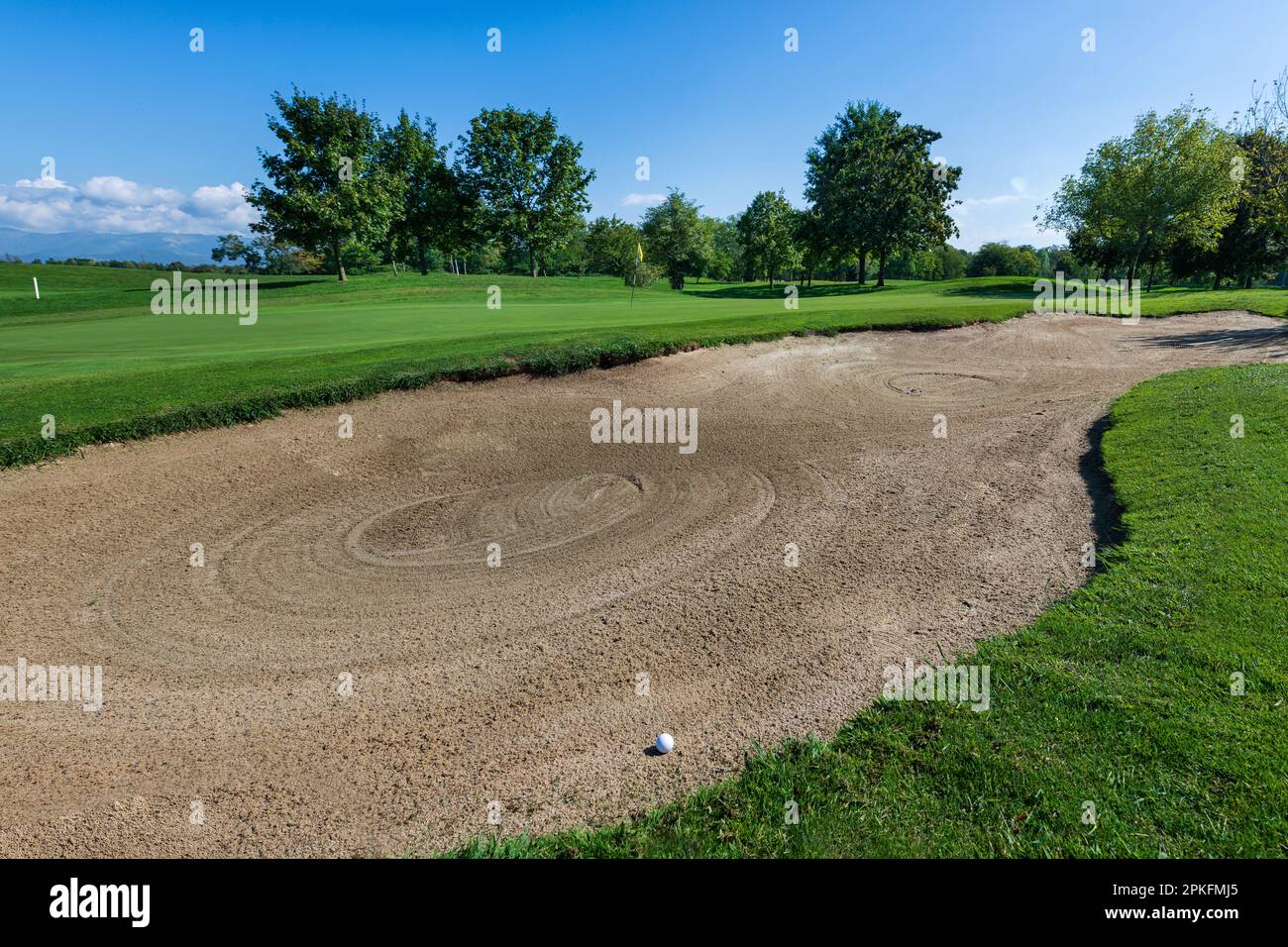 Ein kleiner Ball, der am Sommertag auf dem Golfplatz auf einem sandigen Bunkerboden feststeckte Stockfoto