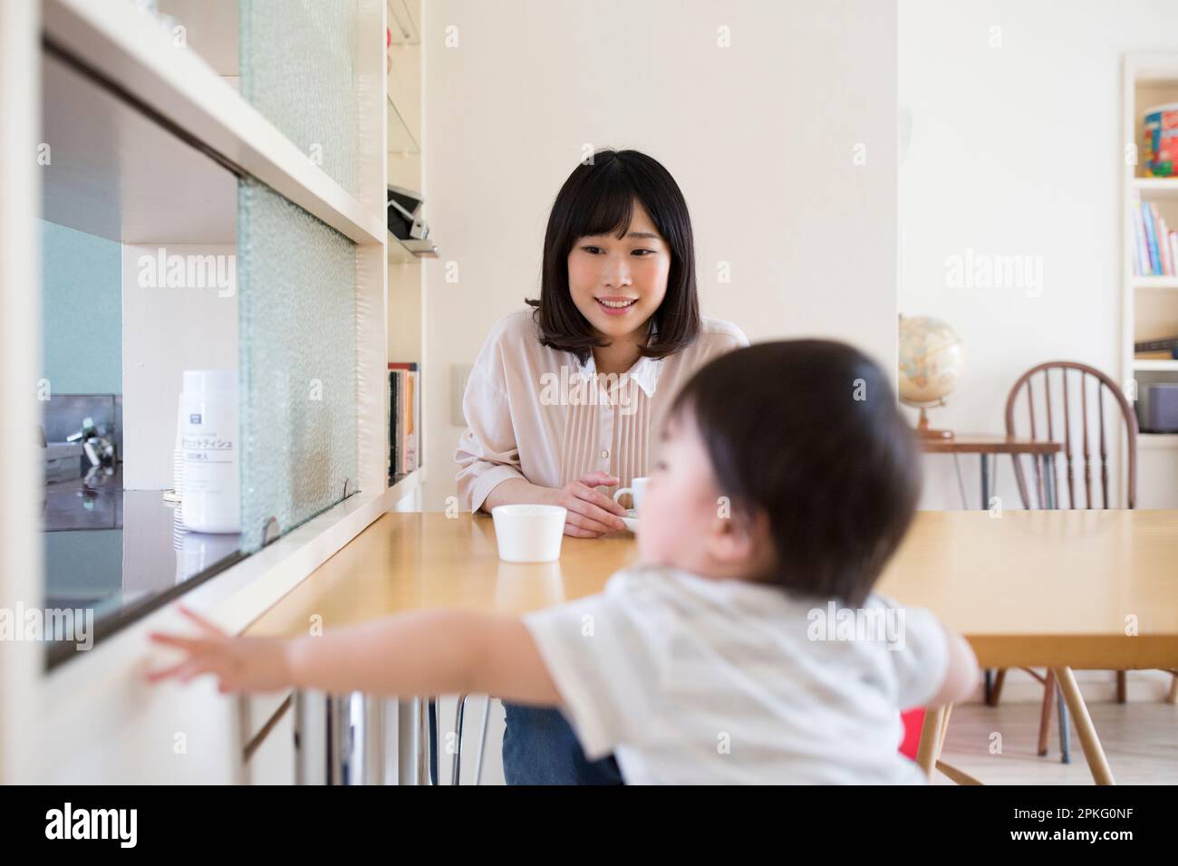 Mutter entspannt sich am Esstisch mit einer Tasse Tee und ein kleiner Junge spielt vor ihr Stockfoto