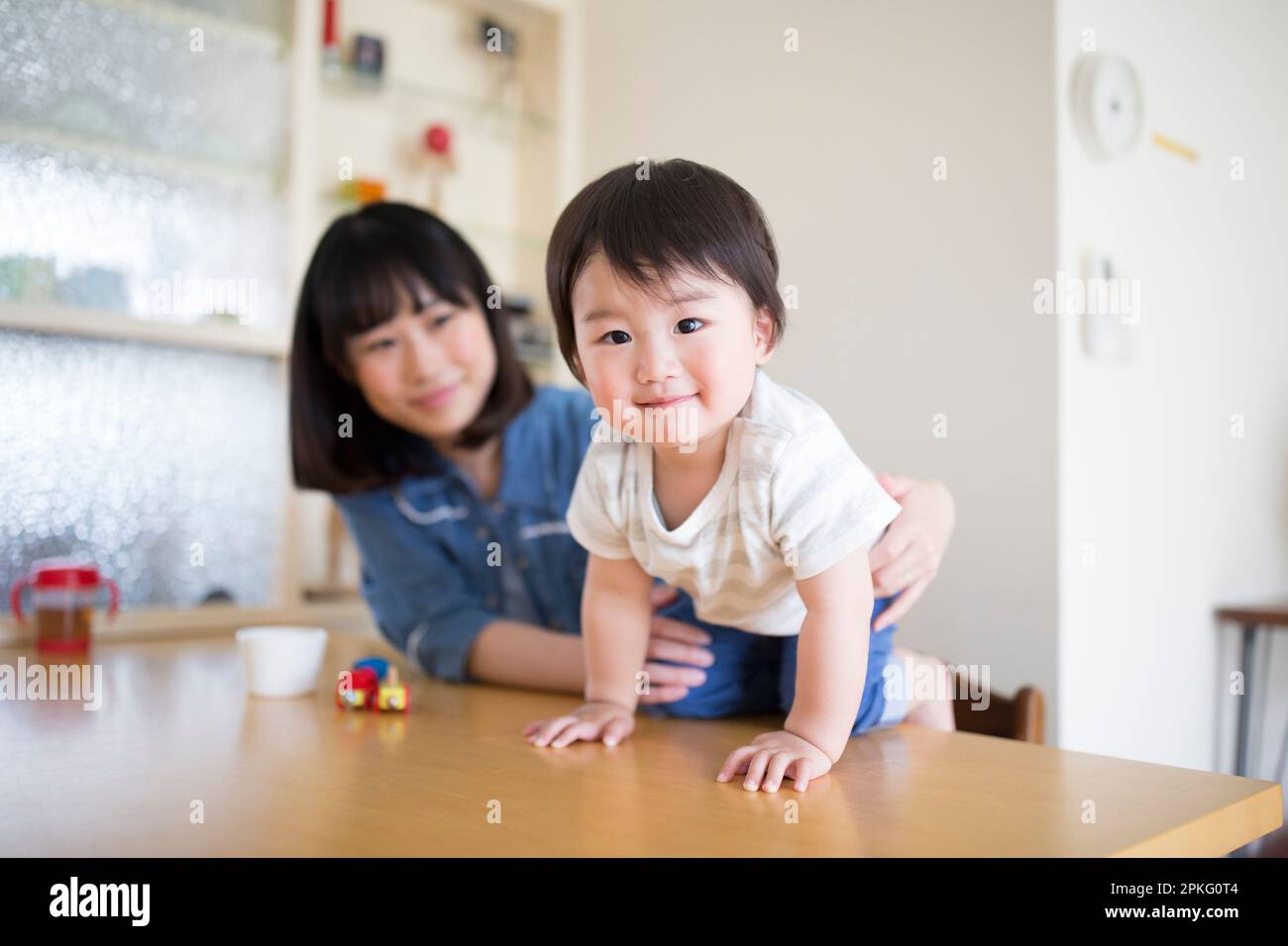 Das Kleinkind lehnt sich über den Esstisch und die Mutter unterstützt ihn Stockfoto
