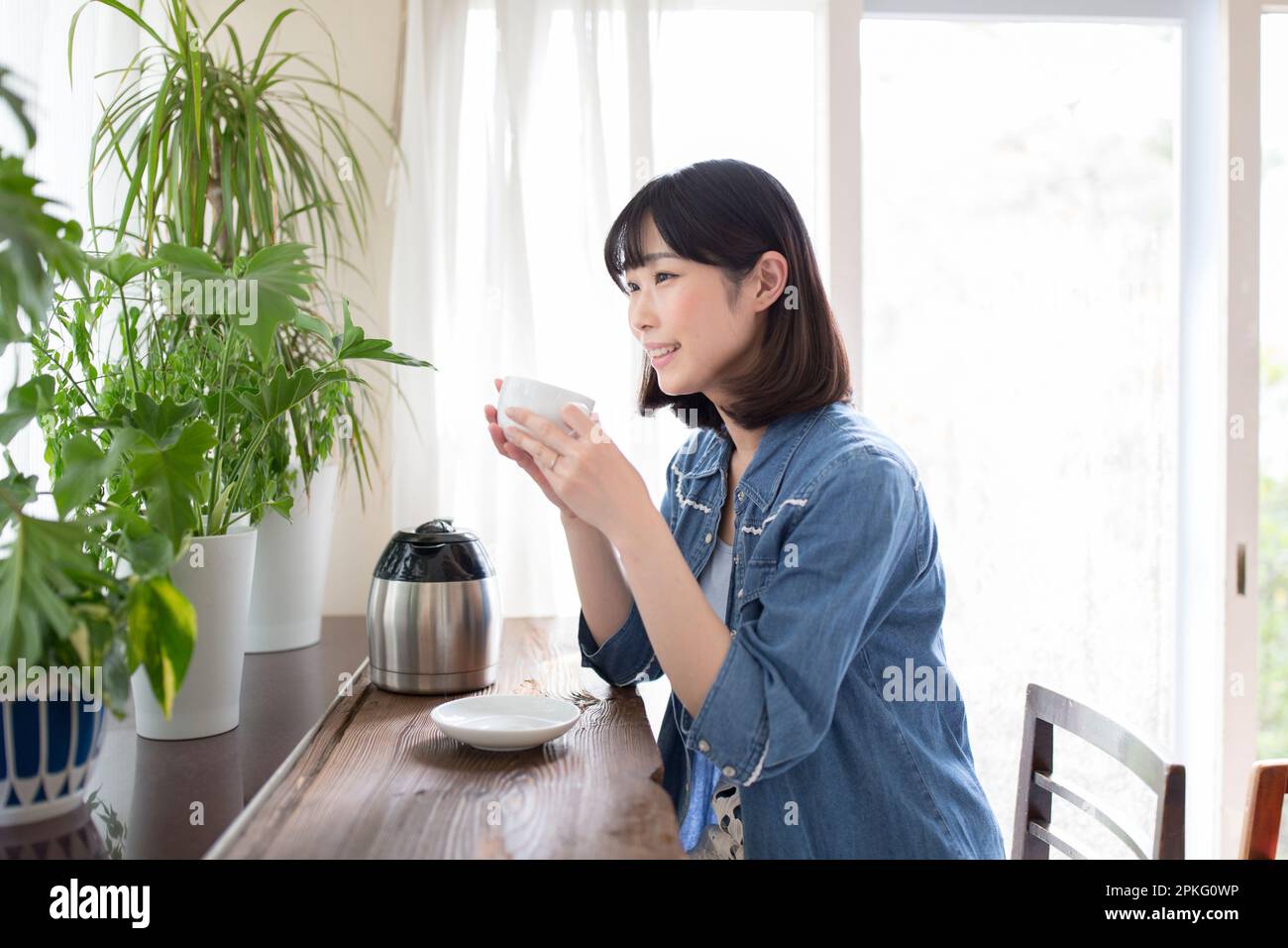 Frau entspannt sich mit Kaffee, während sie sich Zimmerpflanzen ansieht Stockfoto
