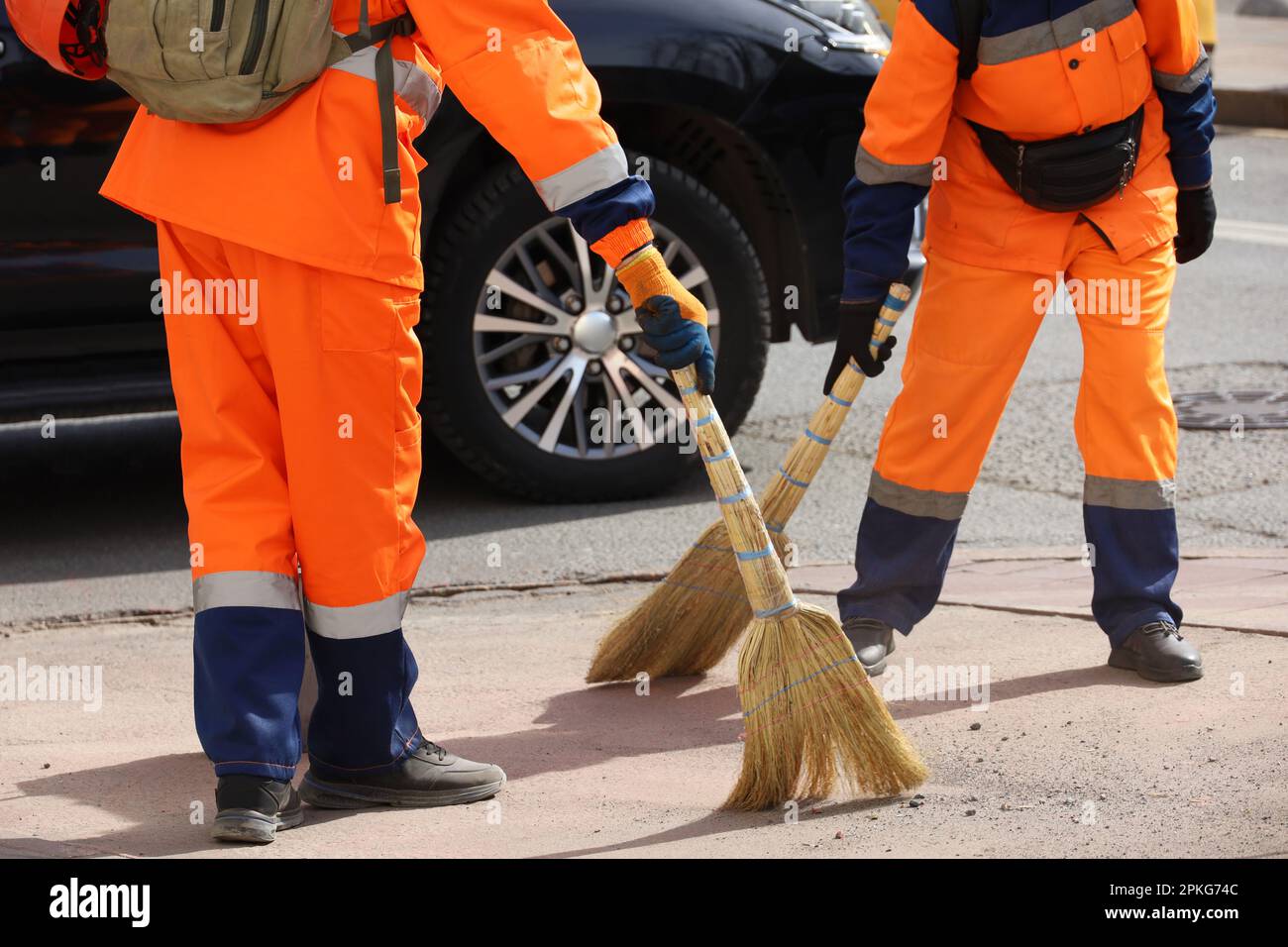 Zwei Hausmeister in orangefarbener Uniform durchkämmen die Straße im Autohintergrund. Putz-Frühjahrsstadt Stockfoto