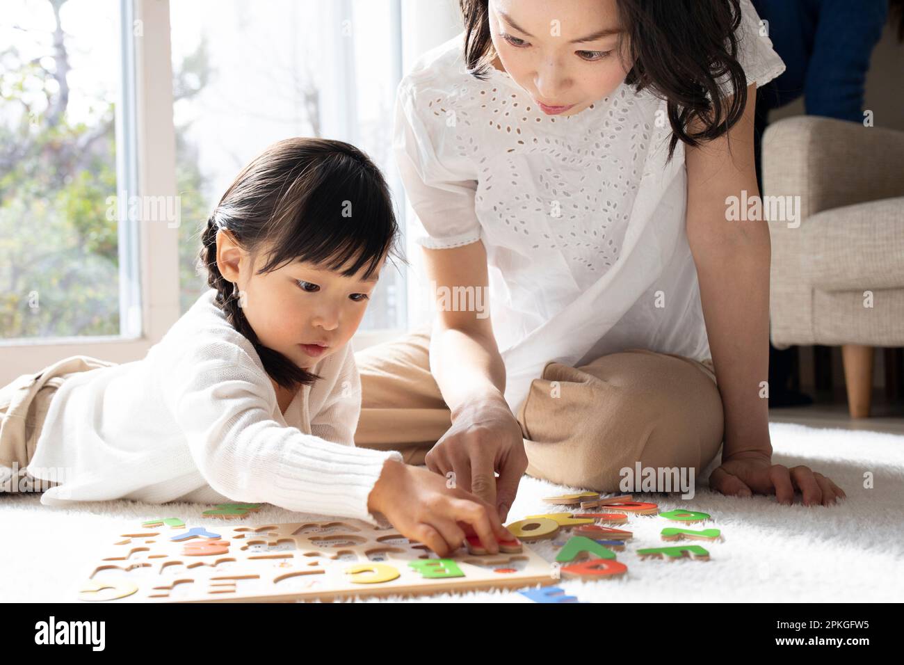 Ein Mädchen, das ein englisches Puzzle macht, und ihre Mutter hilft ihr Stockfoto
