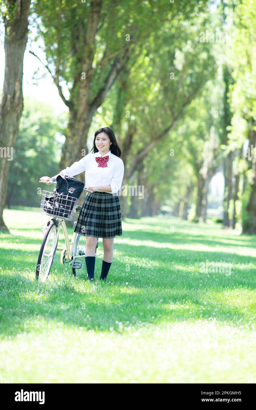 Studentin, die ein Fahrrad auf eine Reihe Pappelbäume schiebt Stockfoto