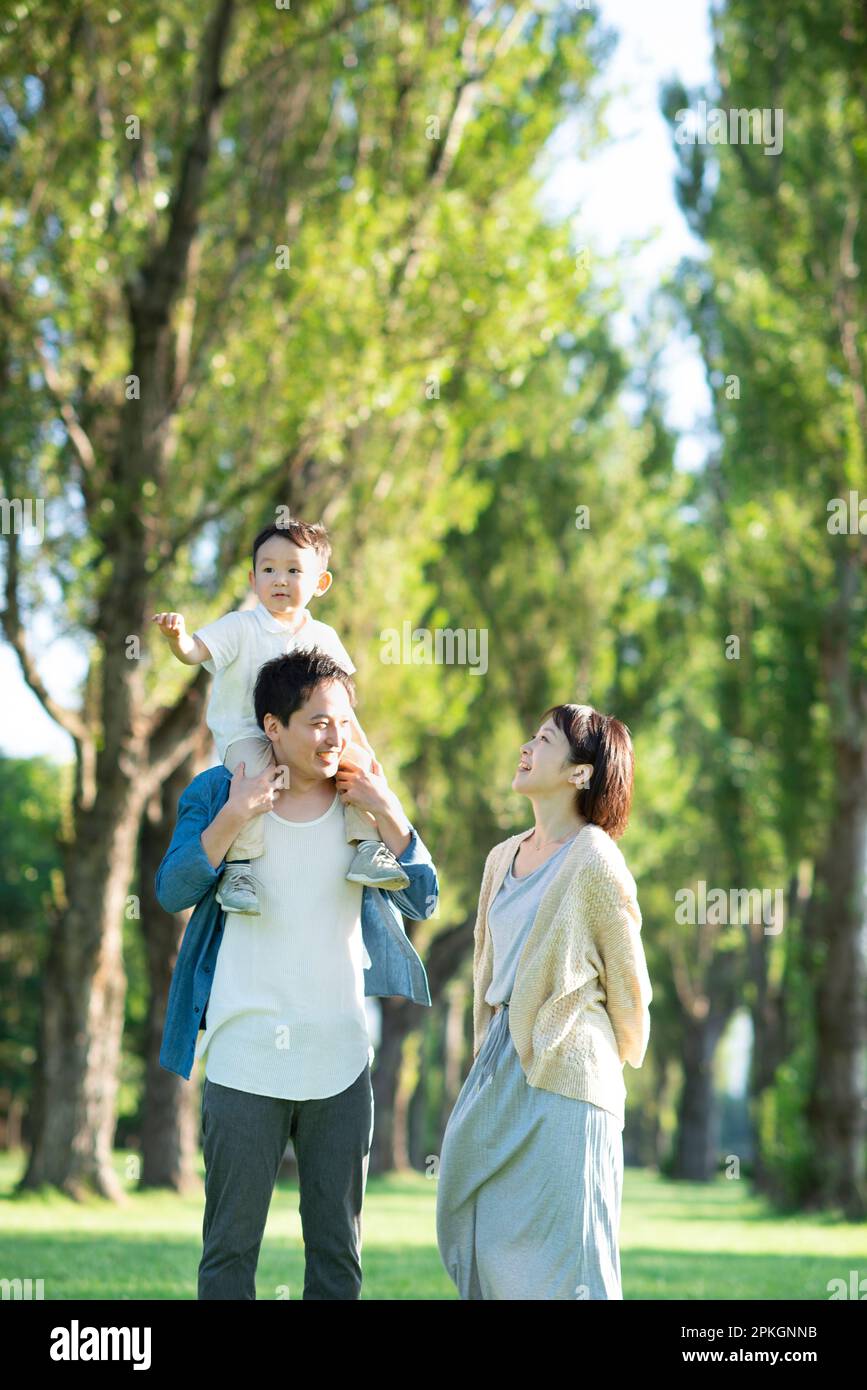 Familie, die ein Kind auf den Schultern in einer Reihe von Pappelbäumen trägt Stockfoto