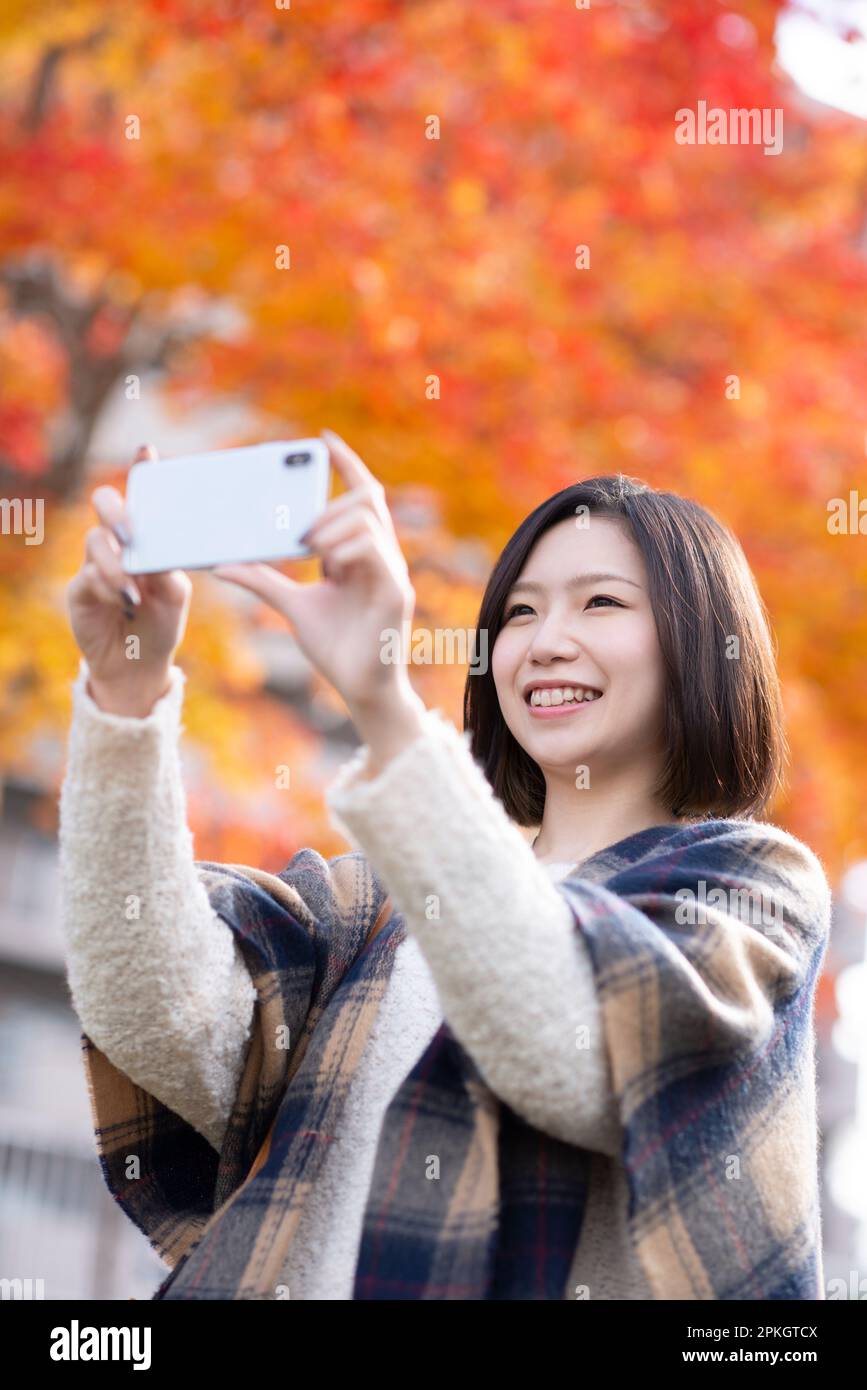 Frau, die mit einem Smartphone ein Bild von Herbstblättern macht Stockfoto
