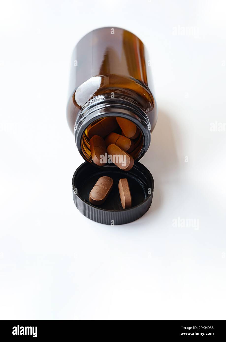 Vitaminkapseln, die Pillen aus der bernsteinfarbenen Glasflasche auf weiß auslaufen lassen. Natürliche Ergänzung für Wellness, Behandlung und Unterstützung für die Gesundheit. Stockfoto