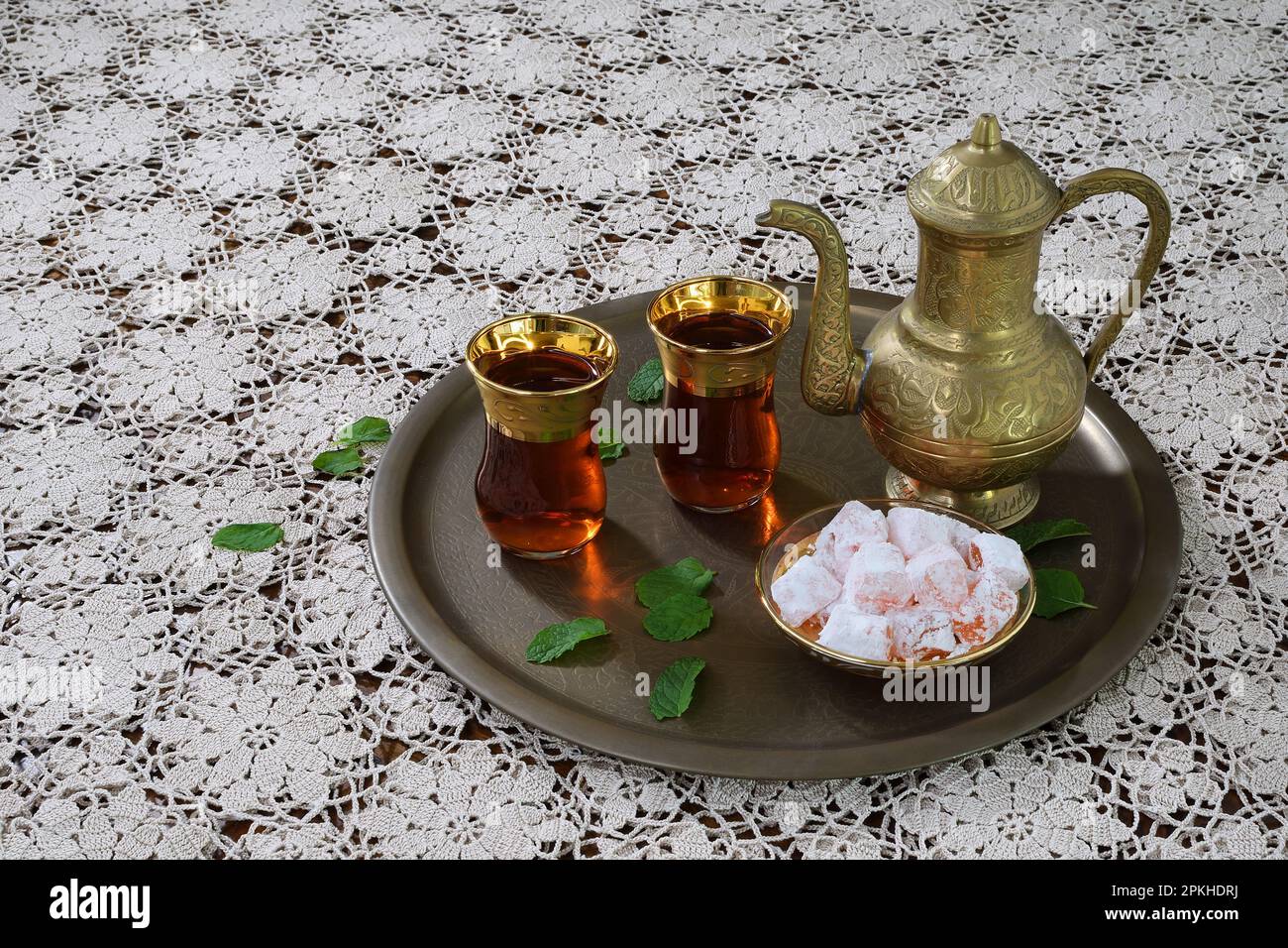 Eine klassische, feierliche, kunstvoll verzierte türkische Teekanne, zwei Gläser und traditionelle türkische Köstlichkeiten auf einem Tablett und weiße Tischdecke aus Spitze in sanfter Beleuchtung Stockfoto