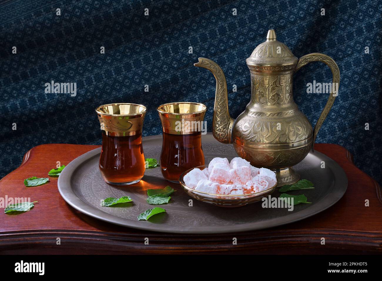 Eine klassische, feierliche, kunstvoll verzierte türkische Teekanne, zwei Gläser und traditionelle türkische Köstlichkeiten auf einem Tablett und einem Holztisch in sanfter stimmungsvoller Beleuchtung Stockfoto