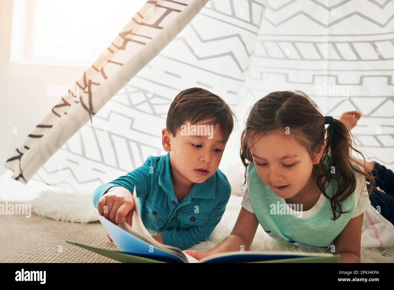 Entdecken Sie die magischsten Orte durch Lesen. Zwei bezaubernde, junge Geschwister, die zu Hause zusammen ein Buch lesen. Stockfoto