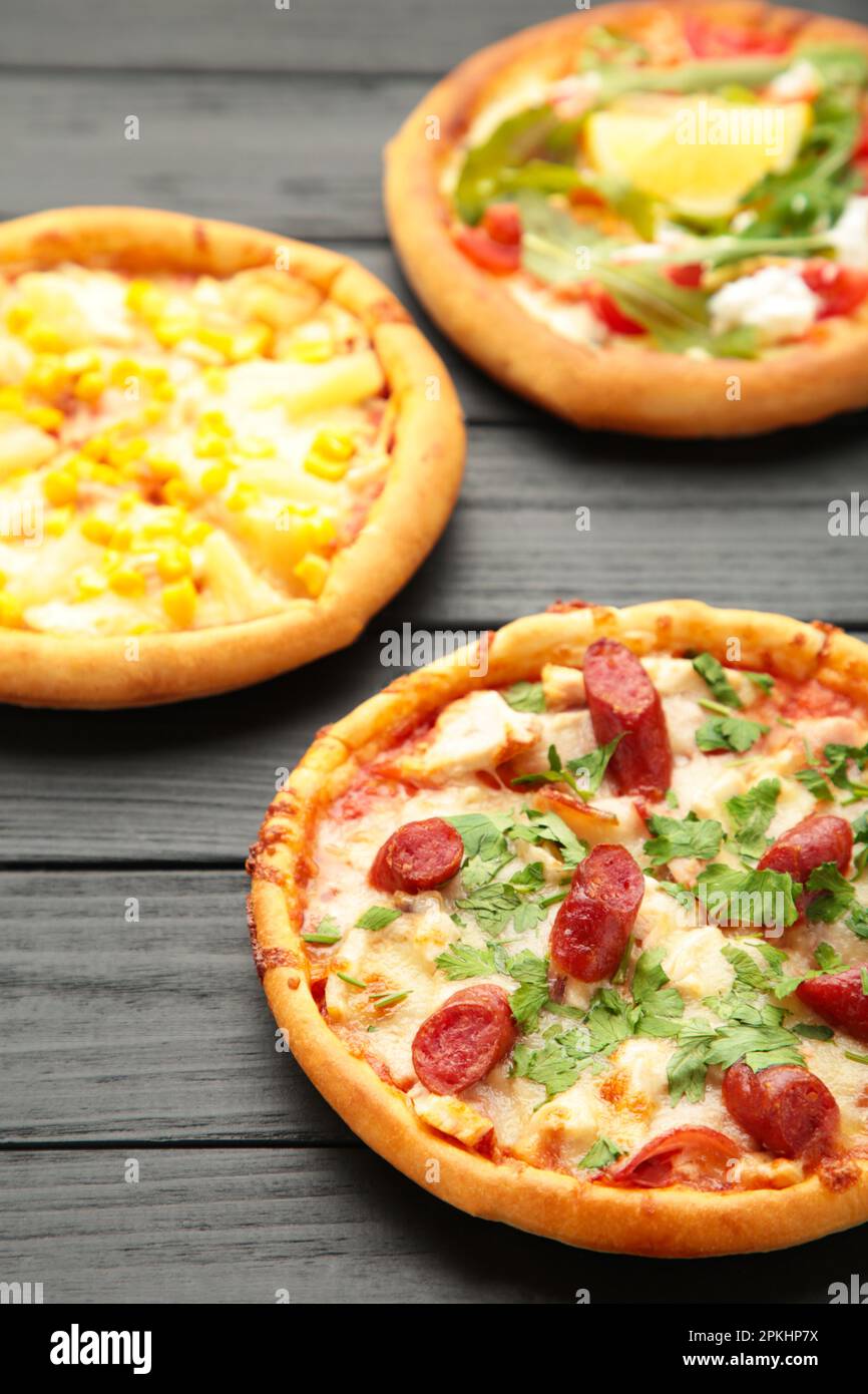 Drei verschiedene Pizzasorten auf einem schwarzen Holztisch. Vertikales foto. Draufsicht Stockfoto