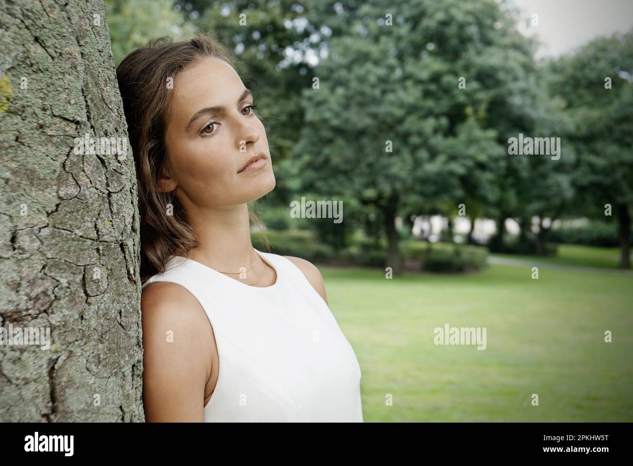 Traurige junge Frau lehnt sich mit Retro-Filtereffekt gegen den Baum Stockfoto