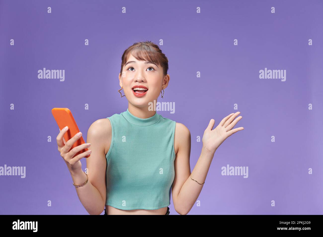 Glückliche asiatische Frau, die sich glücklich fühlt und steht, halten Sie das Smartphone mit der anderen Hand auf lila Hintergrund offen Stockfoto