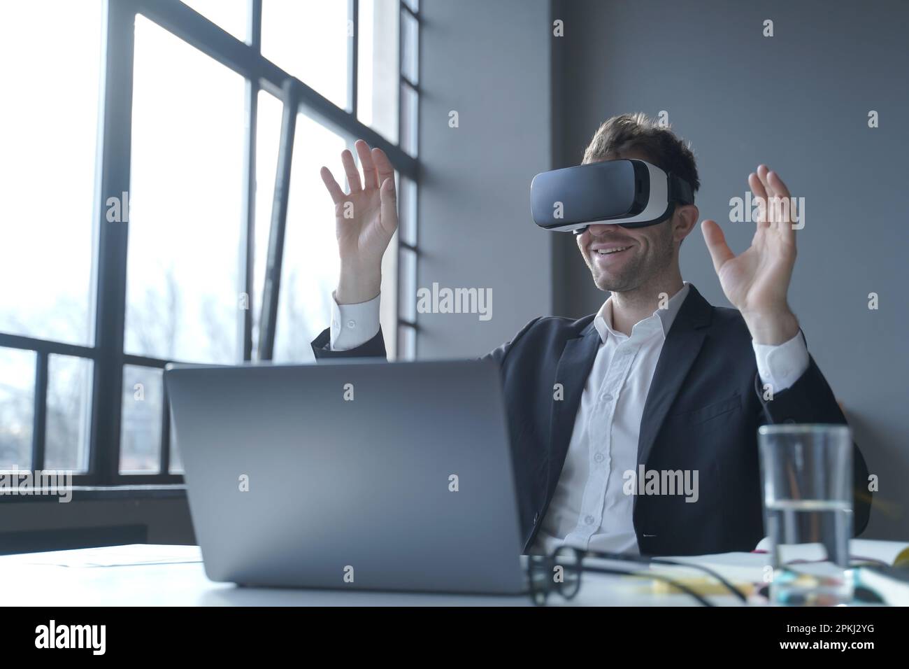 Mitarbeitererfahrung mit virtueller Realität. Junger Geschäftsmann im Anzug, sitzt am Bürotisch und benutzt eine Brille auf der Arbeit, männlicher Unternehmer Stockfoto