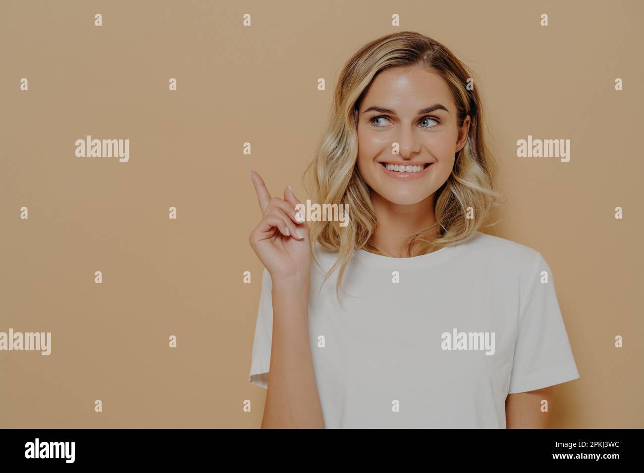 Sieh dir das an. Positive junge Kundin mit blondem Haar, die ein weißes T-Shirt trägt, mit einem angenehmen Lächeln, das auf den Kopierbereich auf orangefarbenem Hintergrund zeigt. Erw Stockfoto