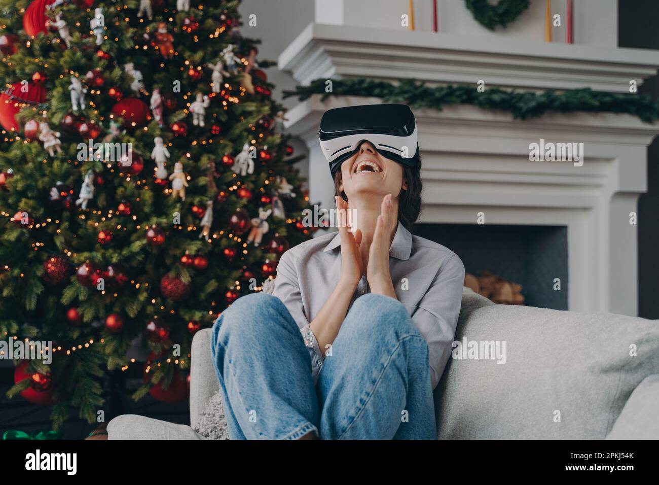 Aufgeregte Frau mit VR-Headset-Brille Genießen Weihnachtsferien zu Hause, lachende Frau trägt eine Virtual-Reality-Brille und entspannt sich auf dem gemütlichen Sofa in Livi Stockfoto