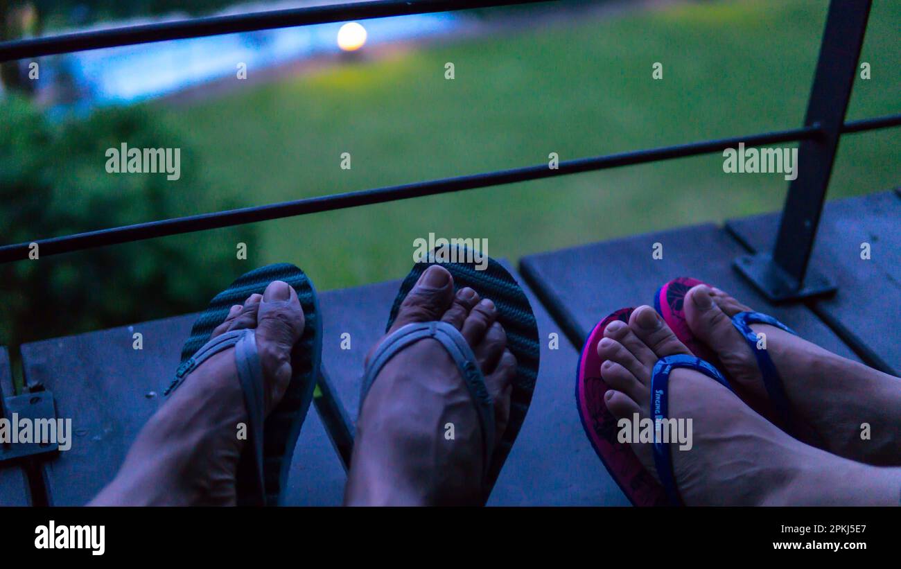 Pärchenbeine in Hausschuhen auf Balkon nachts Stockfoto