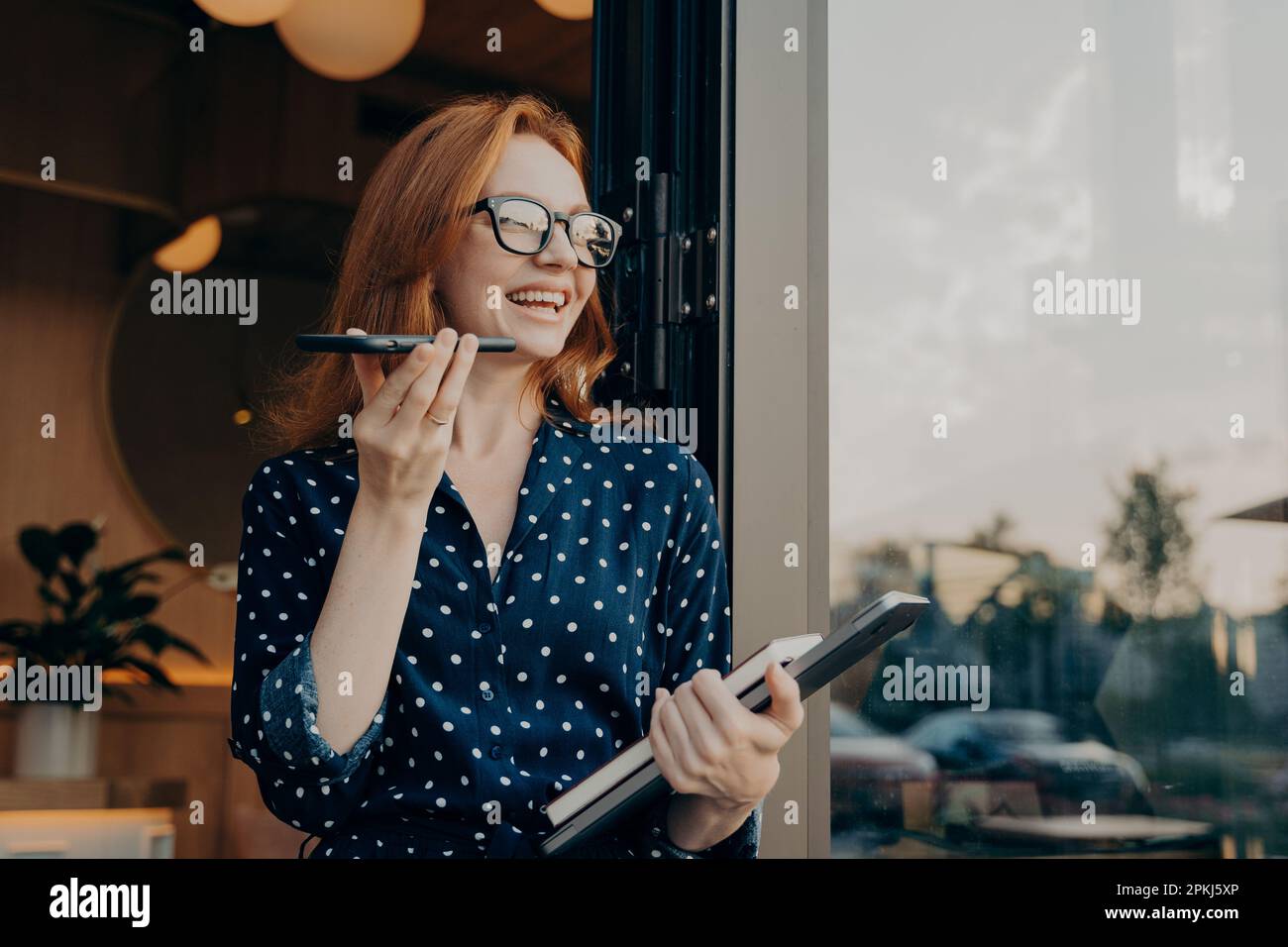 Positiv schöne Frau mit rotem Haar hält Telefongespräche über Freisprechtelefon mit Freund macht Spracherkennung oder Anfrage nutzt Internetdienste Pose n Stockfoto