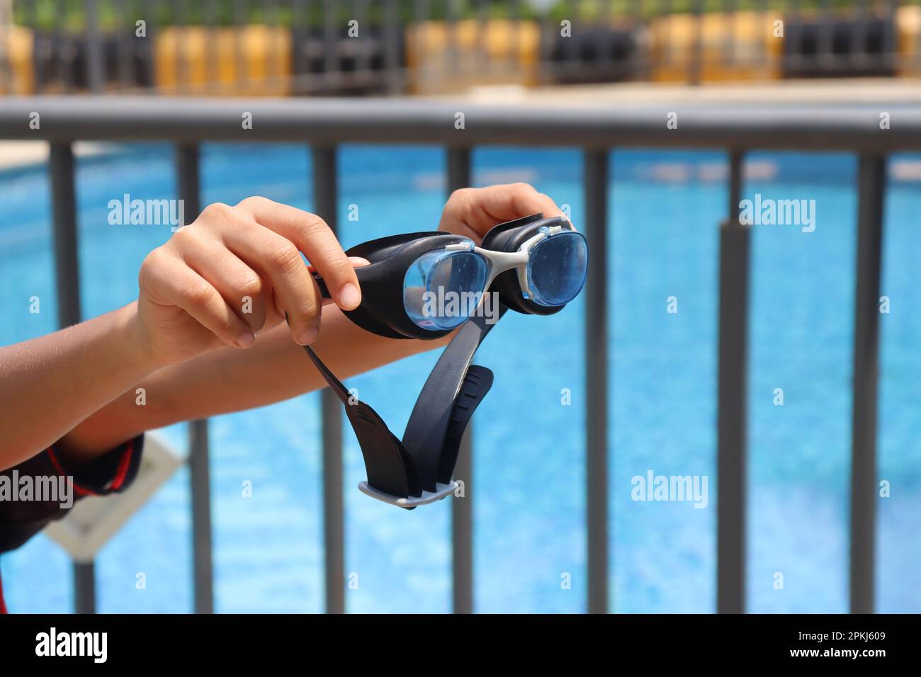 Schwimmbrille in der Hand mit einem Pool im Hintergrund, der das Konzept der Sommeraktivitäten im Freien zeigt Stockfoto