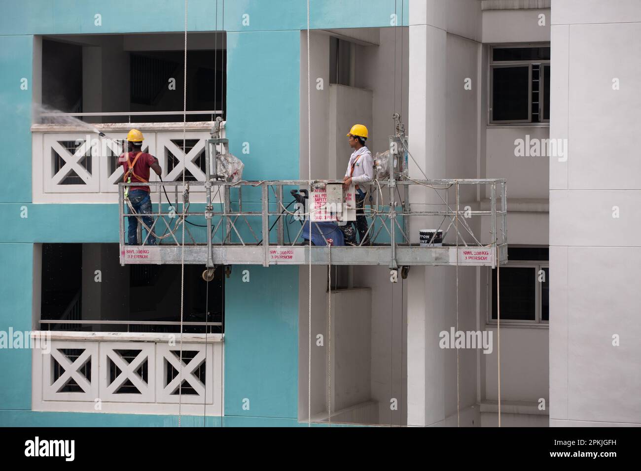 Zwei Arbeiter auf dem Gerüstaufzug, einer, der mit Wasserstrahl den Schmutz von der Außenwand entfernt, und der andere, der die Höhe steuert. Stockfoto