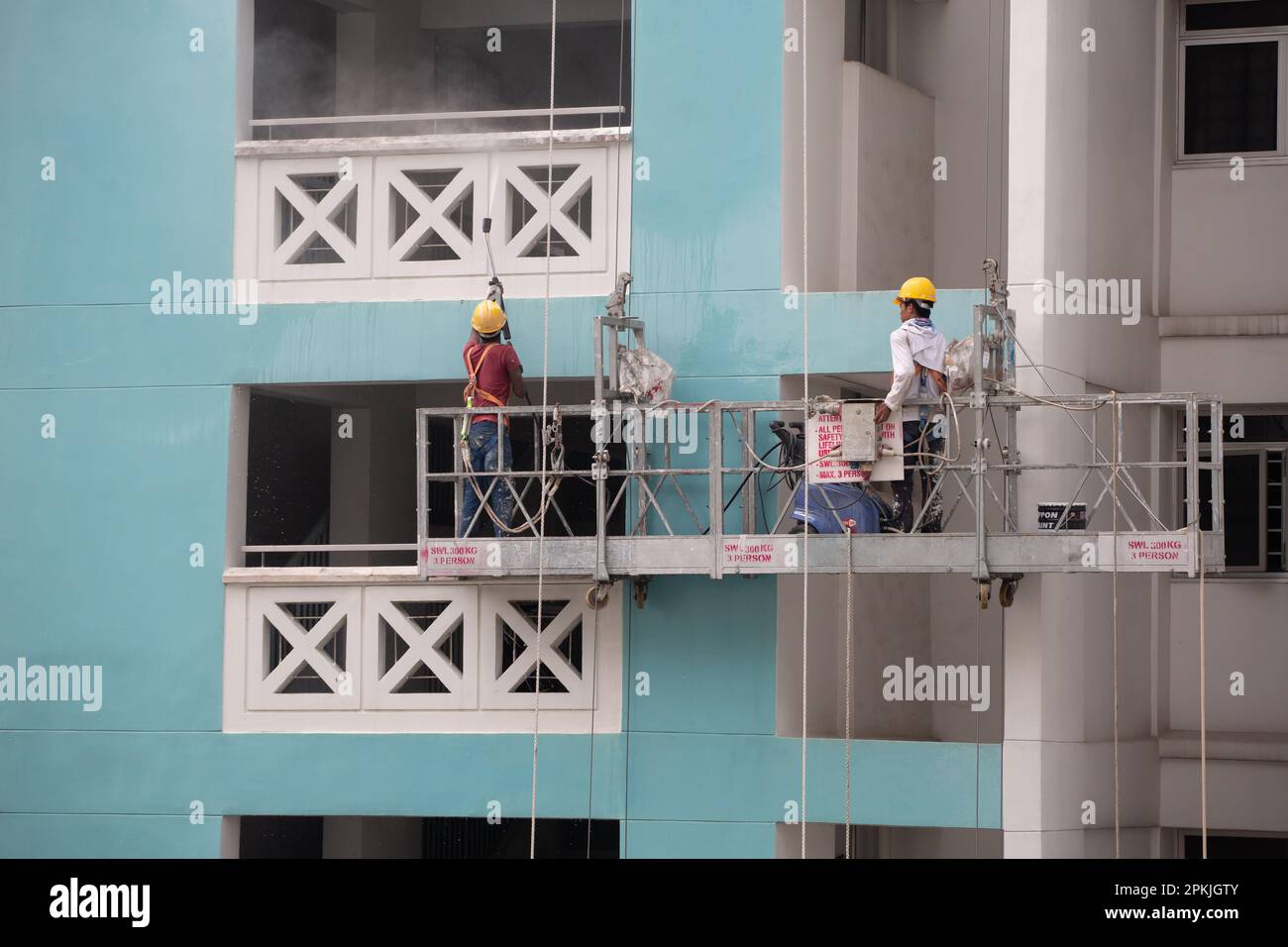 Zwei Arbeiter auf dem Gerüstaufzug, einer mit Wasserstrahl, um Schmutz von der Außenwand zu entfernen, und der andere steuert die Höhe. Stockfoto