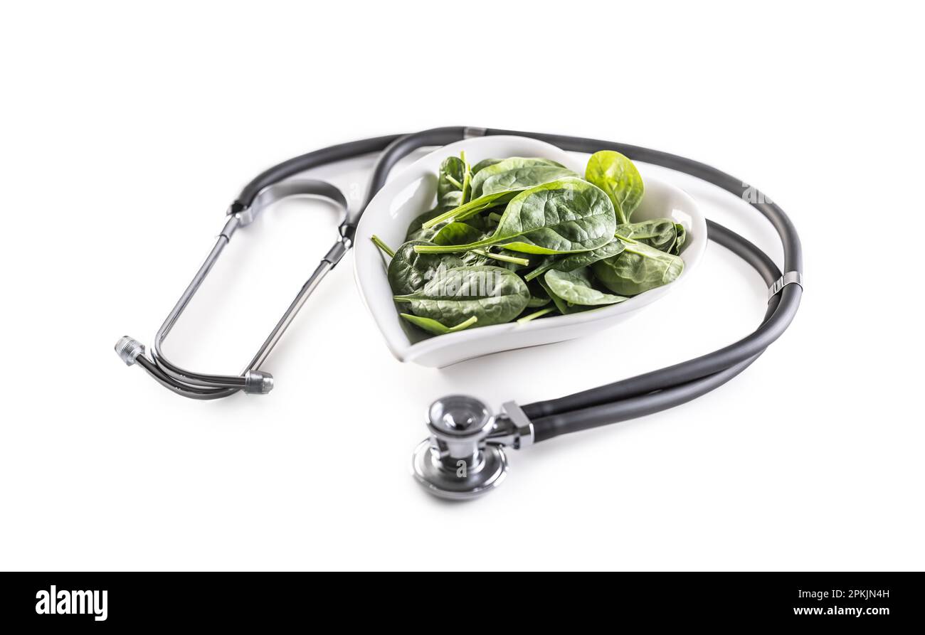 Symbol für gesundes Herz mit Stetoskop und herzförmiger Schüssel voller Baby-Spinat-Blätter auf isoliertem weißem Hintergrund. Stockfoto