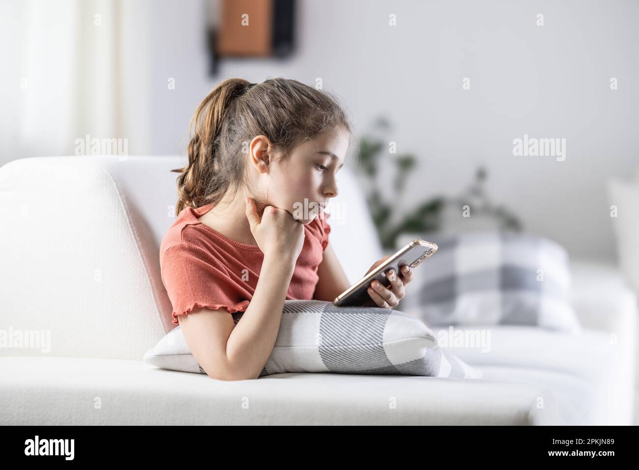 Die junge Generation ist immer auf ihren Telefonen, dargestellt von einem Mädchen zu Hause mit einem Handy in der Hand. Stockfoto