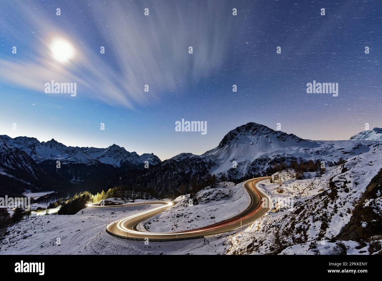 Vollmond über einer verschneiten Bergstraße, beleuchtet von Autowegen, Bernina Pass, Val Poschiavo, Graubunden Kanton, Schweiz, Europa Stockfoto