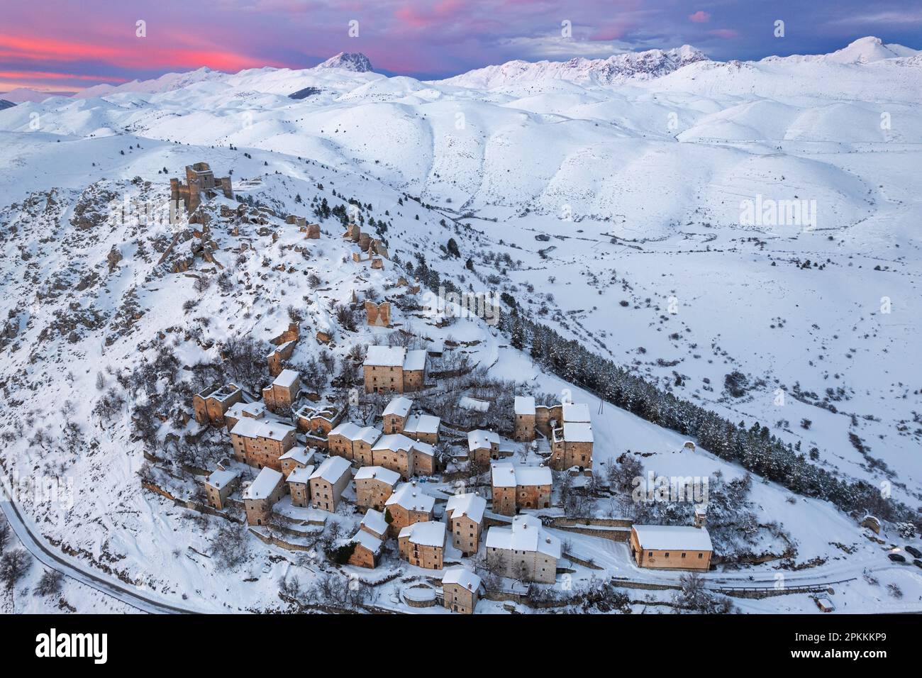 Unvergleichlicher Winterblick auf das schneebedeckte mittelalterliche Dorf Rocca Calascio mit Schloss und rosa Himmel bei Sonnenuntergang, Rocca Calascio Stockfoto