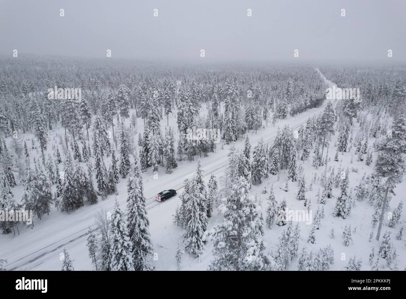 Blick von oben auf ein Auto, das eine eisige Straße inmitten des gefrorenen, mit Schnee bedeckten Waldes, Akaslompolo, Kolari, Pallas-Yllastunturi Nationalpark fährt Stockfoto