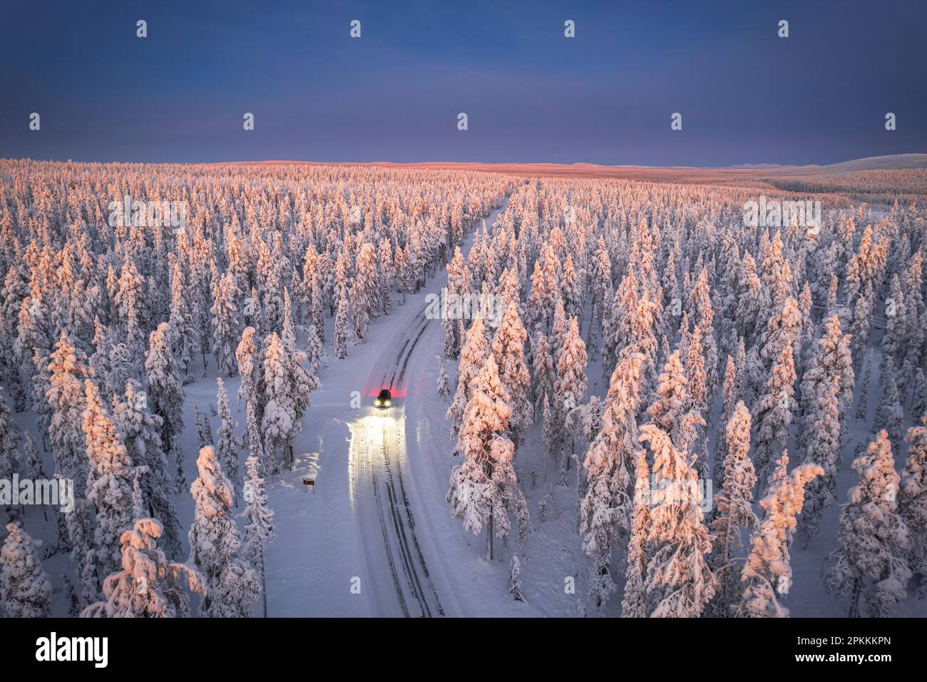 Luftaufnahme des Autos auf vereister Straße und beleuchtete Scheinwerfer im schneebedeckten Wald, Akaslompolo, Kolari, Pallas-Yllastunturi Nationalpark Stockfoto