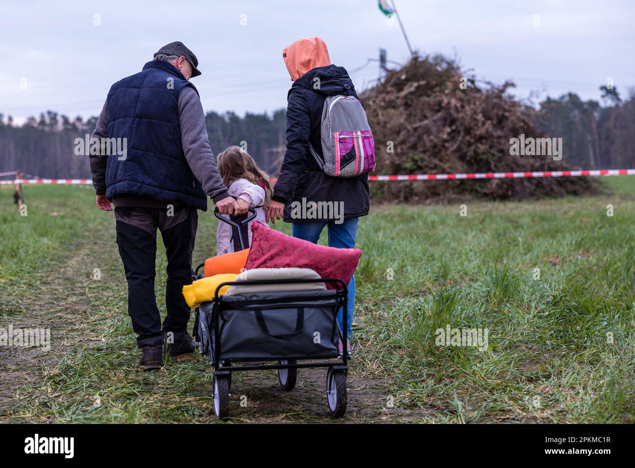 Cottbus, Deutschland. 08. April 2023. Eine Familie kommt mit einem Handwagen zum Osterfeuer in Branitz, das noch nicht angezündet wurde. Die Kameraden der freiwilligen Feuerwehr des Cottbus-Bezirks Branitz hatten etwa 25 Kubikmeter Holzabfälle von den Bewohnern und Handwerkern gesammelt und am Morgen des heutigen Heiligen Samstags in einen Holzhaufen gestapelt. Mehrere hundert Besucher kamen zum Osterfeuer. Kredit: Frank Hammerschmidt/dpa/Alamy Live News Stockfoto