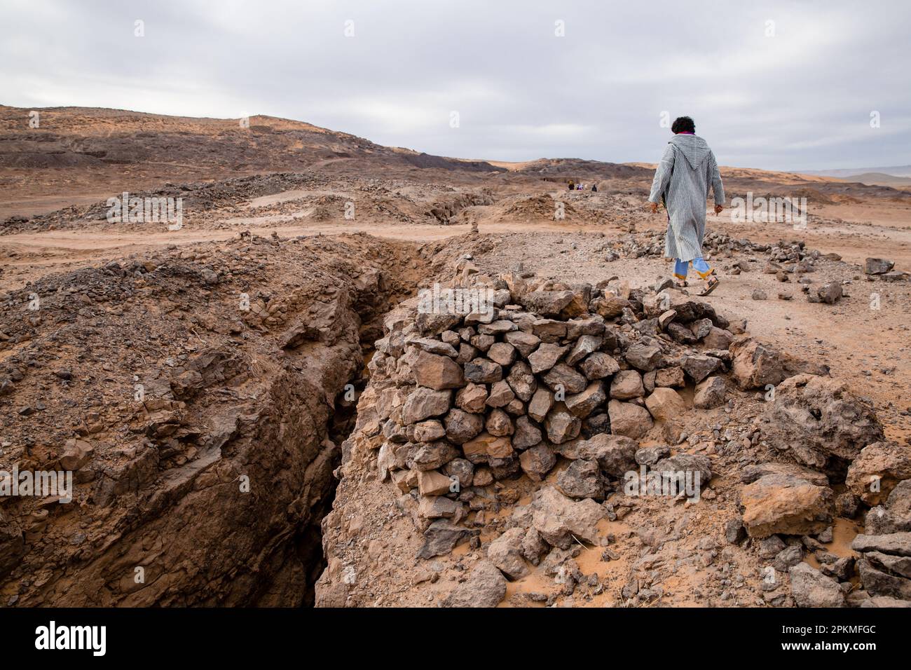 Ein Berber mit einer Djellaba geht in der Wüste zwischen Steinen spazieren Stockfoto