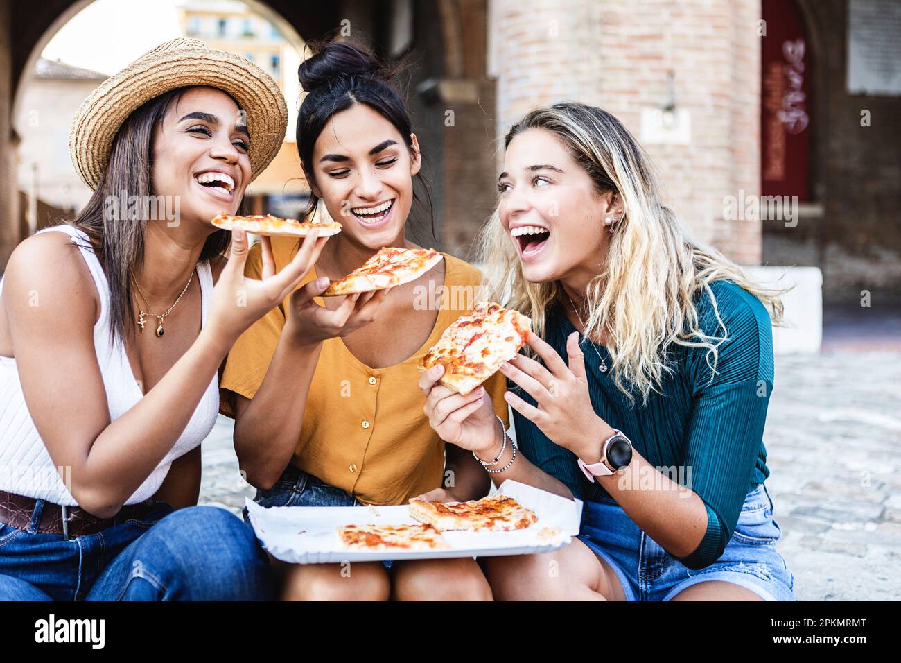 Drei junge, glückliche Frauen, die Pizza essen und sich in den Sommerferien in Italien Vergnügen Stockfoto