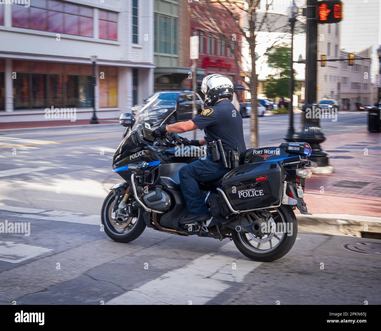 Ein Polizist auf einem schwarzen Motorrad, der einen Helm und eine volle Uniform trägt, wird gesehen, wie er im Dienst auf einer belebten Straße der Stadt fährt. Stockfoto