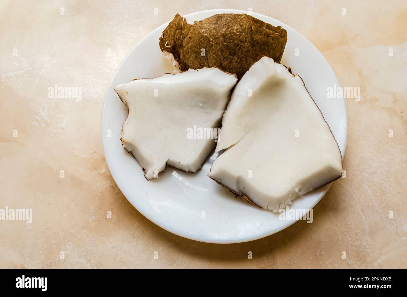 Drei Stücke einer trockenen Kokosnuss liegen auf einem weißen Teller auf einer weißen gefliesten Arbeitsfläche. Stockfoto