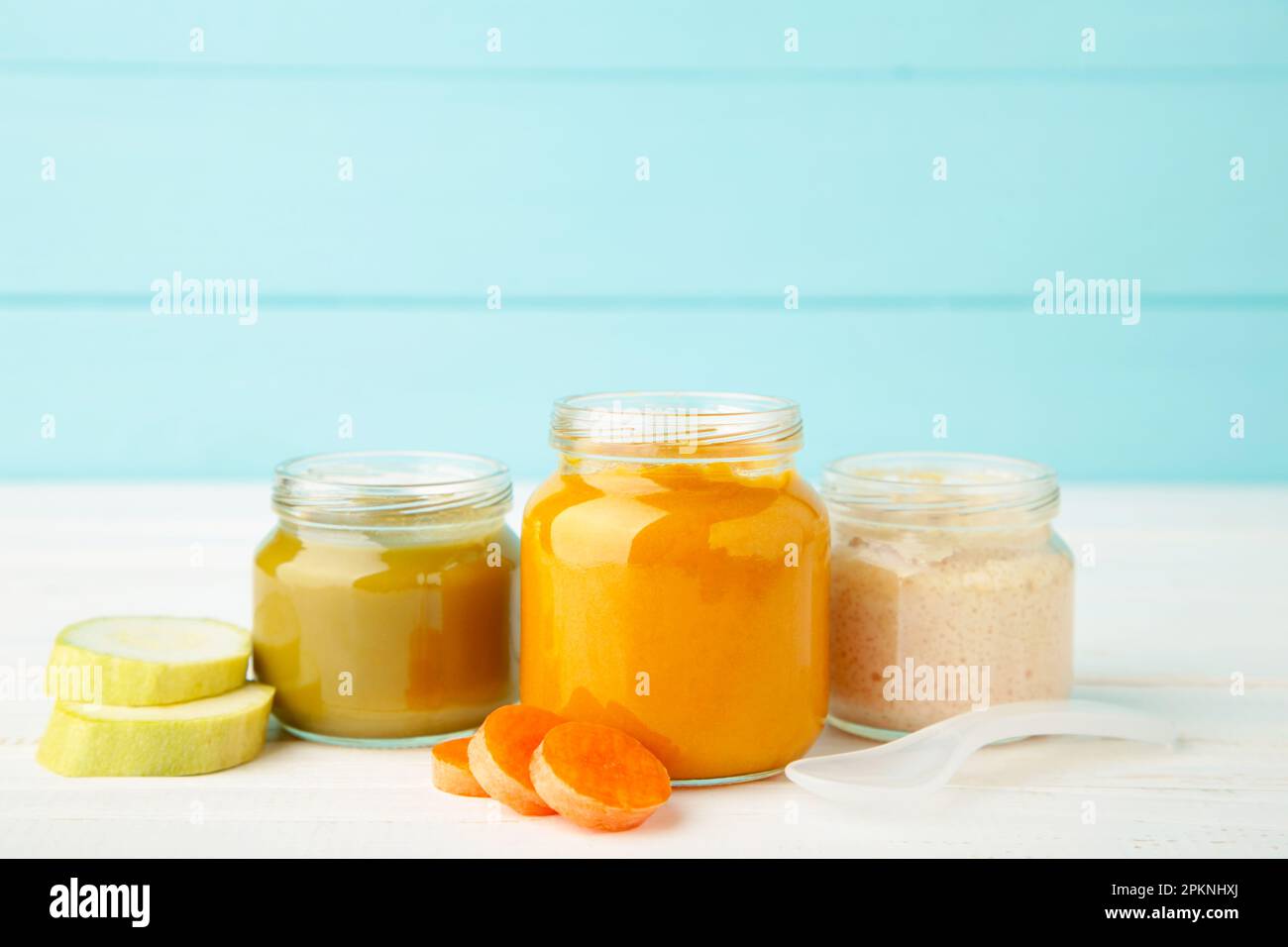 Glasgefäße mit nährstoffhaltiger Babynahrung auf blauem Hintergrund. Gemüsepüree mit Löffel. Stockfoto