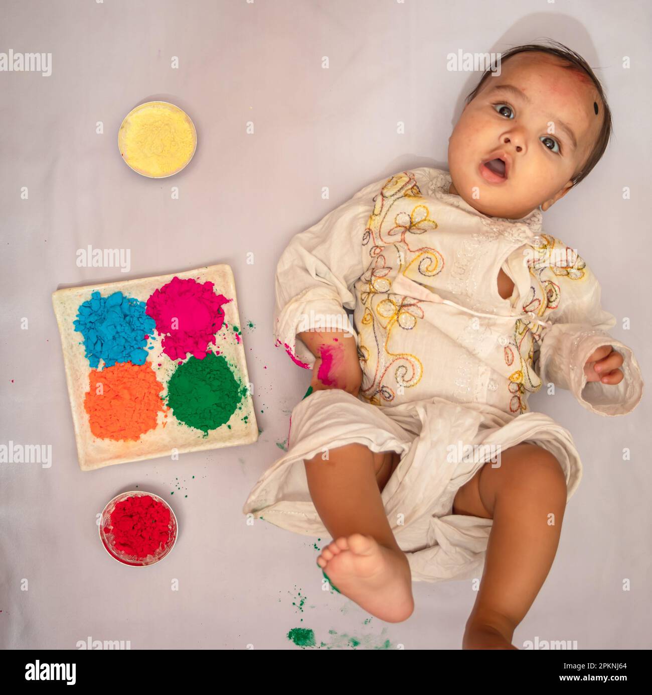 Kleinkind liegt im Bett und zahlt holi in traditioneller Kleidung mit mehrfarbigen Farben aus dem oberen Winkel Stockfoto