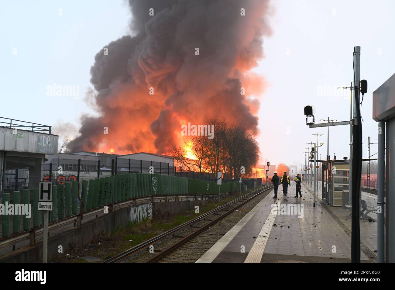 Hamburg, Deutschland. 09. April 2023. Polizeibeamte halten am Bahnhof Hamburg-Rothenburgsort, während im Hintergrund Flammen eines Großbrandes zu sehen sind. Aufgrund der starken Rauch- und Gasentwicklung mit möglichen chemischen Komponenten hat die örtliche Polizei eine offizielle Gefahrenwarnung ausgegeben. Kredit: Jonas Walzberg/dpa/Alamy Live News Stockfoto